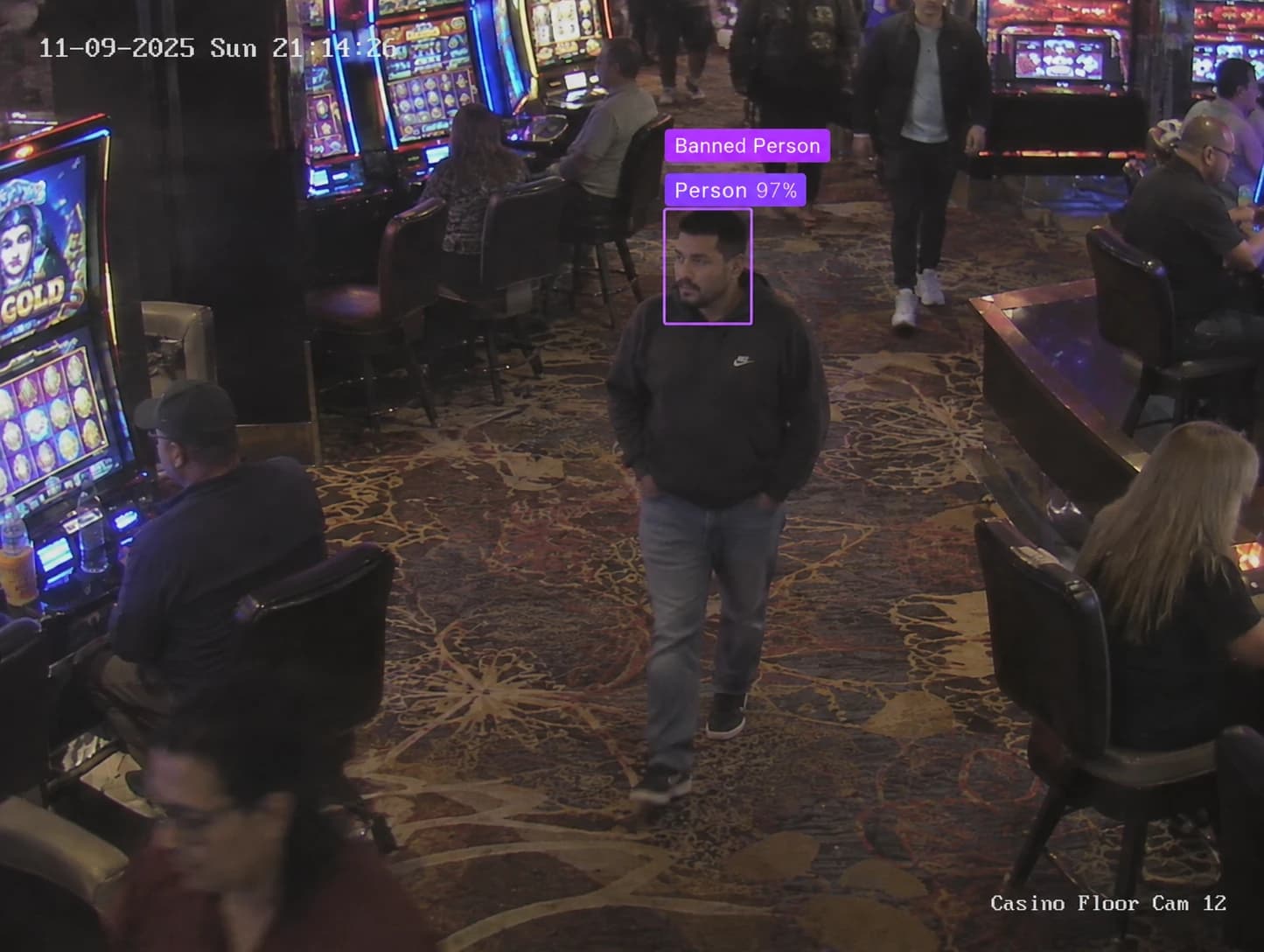 Casino floor camera: a man in a hoodie walking between slot machines, his face boxed and labelled Banned Person