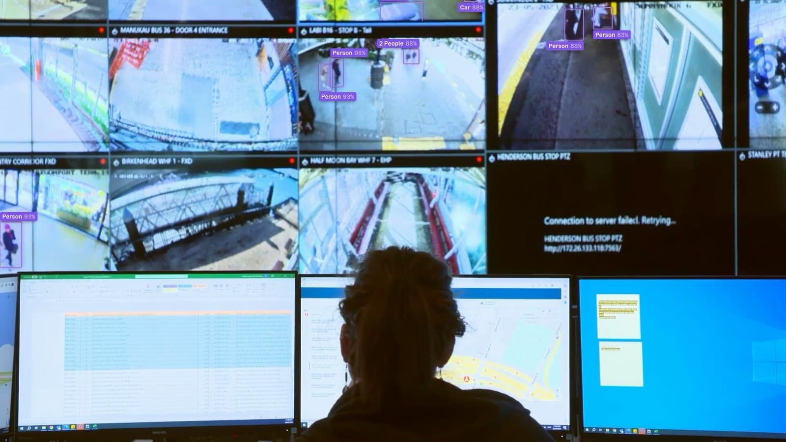 An operator in a security control room watching a wall of camera feeds